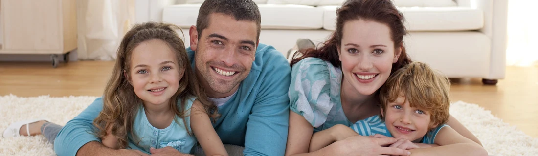 Happy Mother and Father with Two Children Smiling While Laying on a Rug on the Floor Family Dentistry
